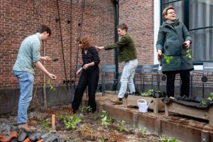 In de tuin van de universiteit maken theologen samen compost. Blik omlaag, handen in de aarde
